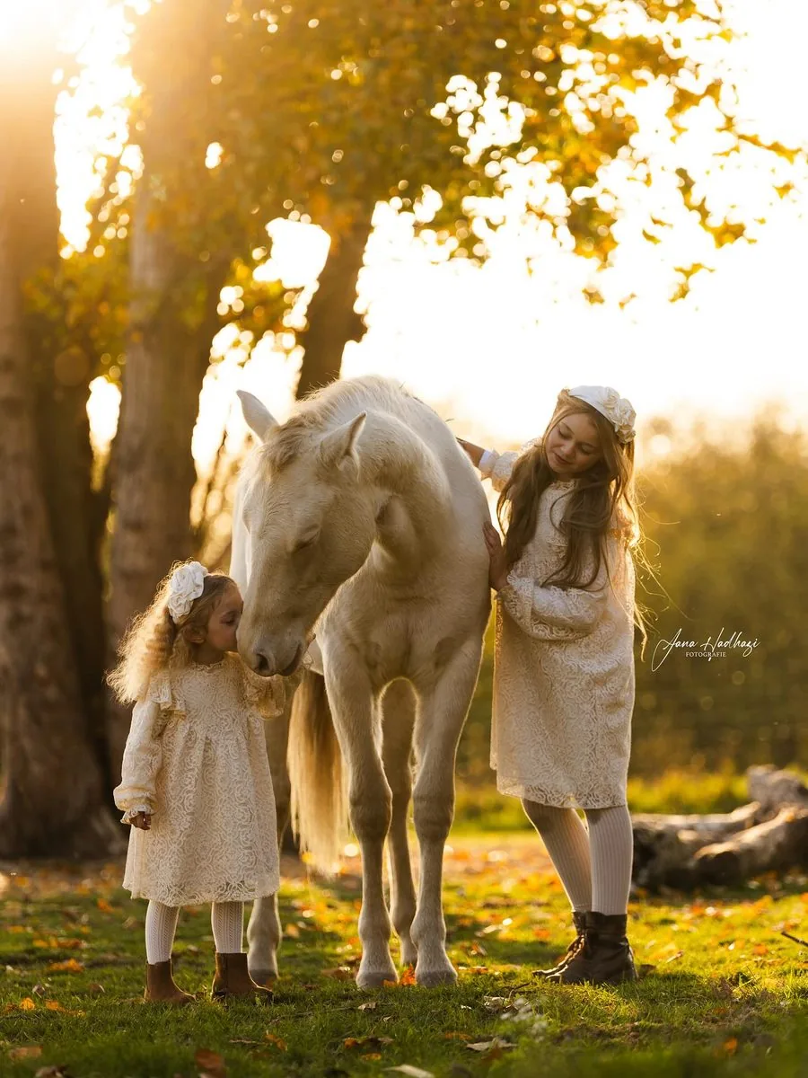 Zwei Mädchen in Spitzenkleidern mit einem hellen Pony im Gegenlicht